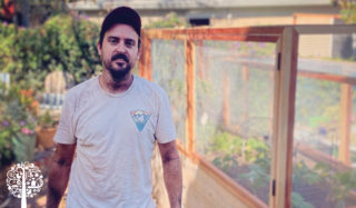 Ο Fernandez στέκεται μπροστά σε ένα ανυψωμένο κρεβάτι στον κήπο στο Victory Garden LA.